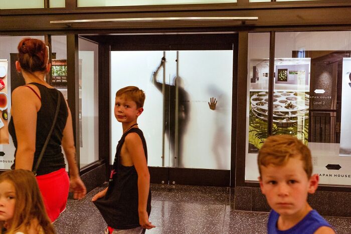 A perfectly timed street photo by Jeremy Paige, showing a boy looking at the camera with a blurred figure in background.
