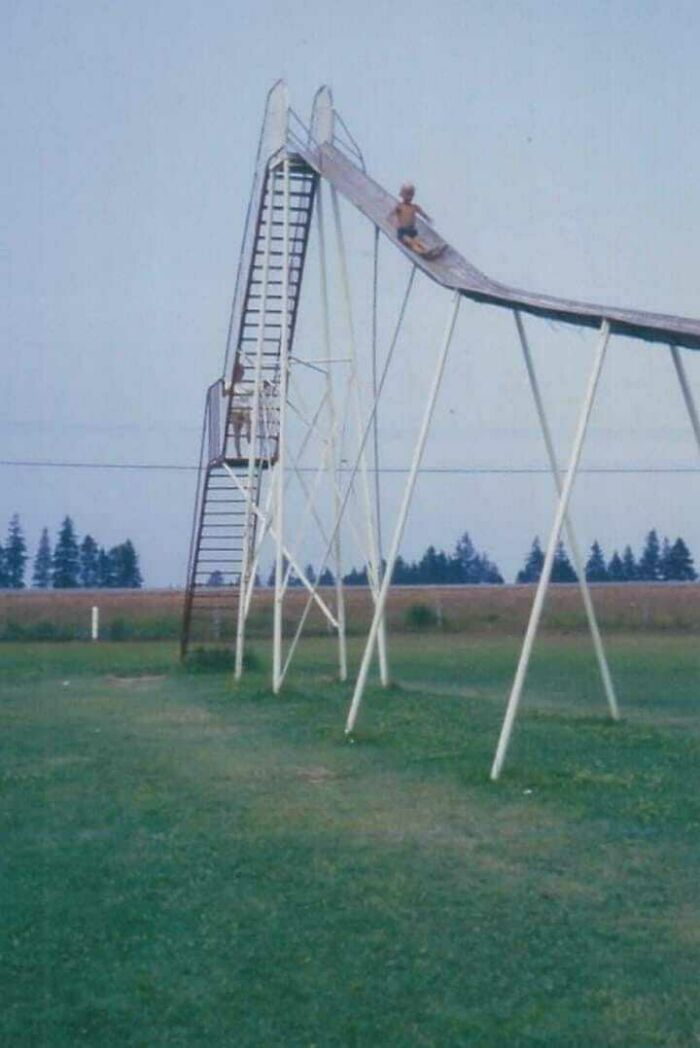 A child at the top of an extremely tall, steep slide in a playground, illustrating playground fails.