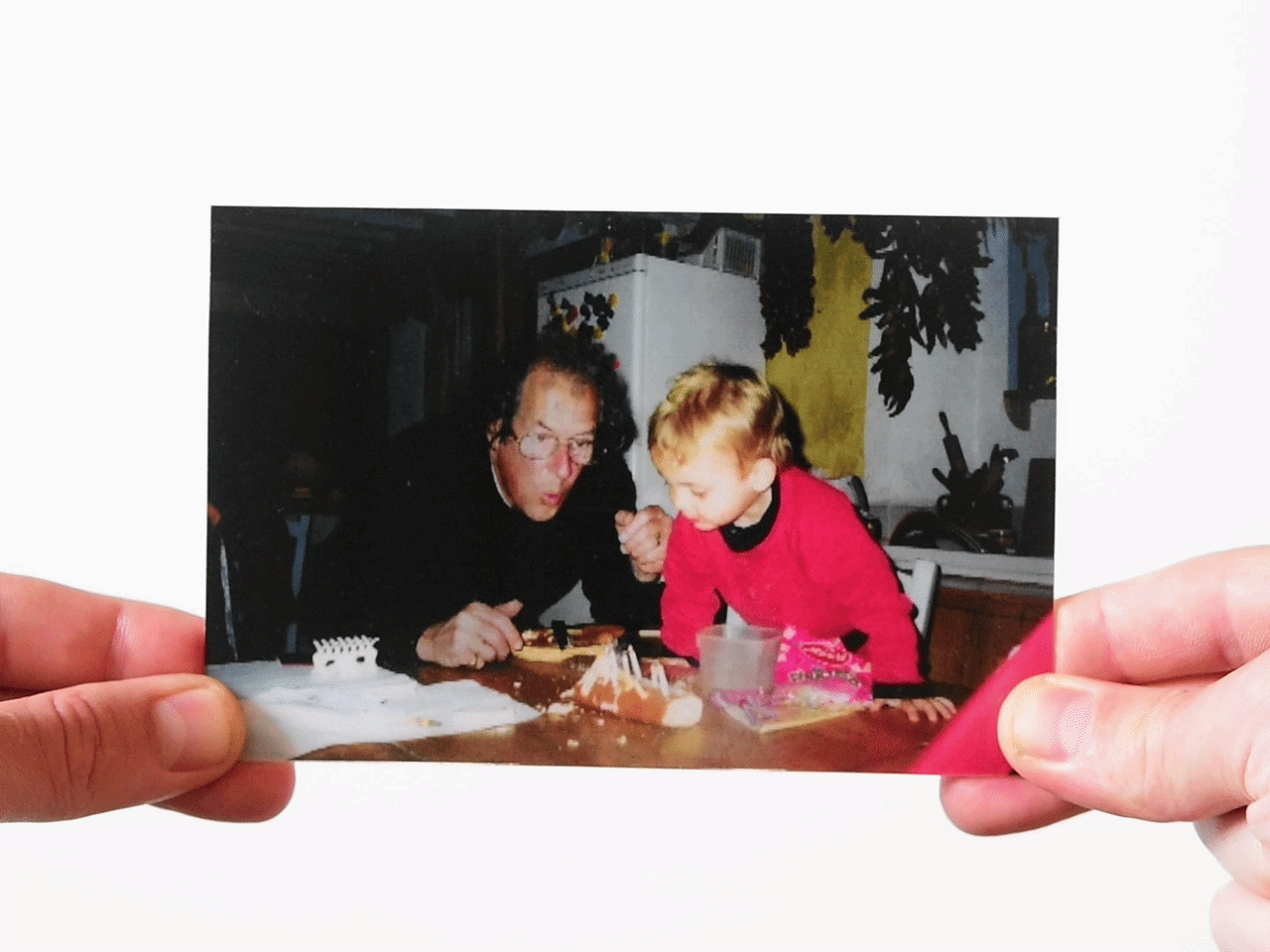 Father blowing out birthday candles held by a child on the table