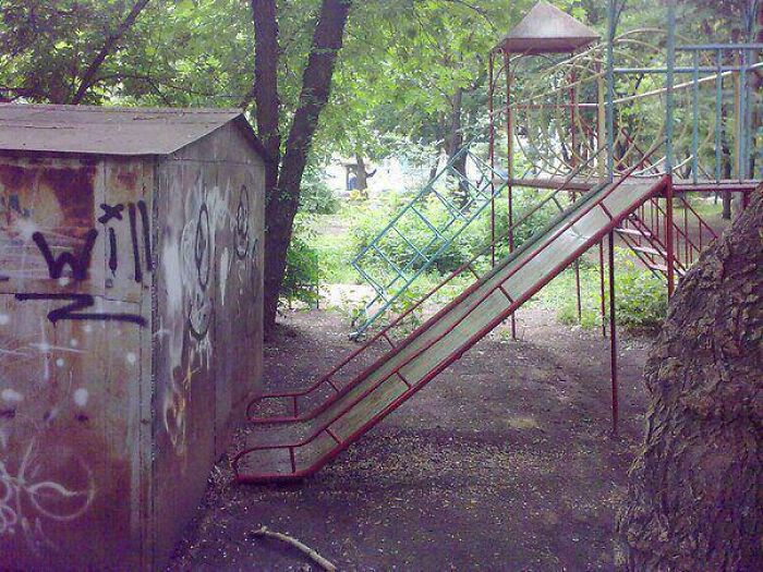 A long, steep playground slide facing a graffiti-covered wall, a clear playground fail.