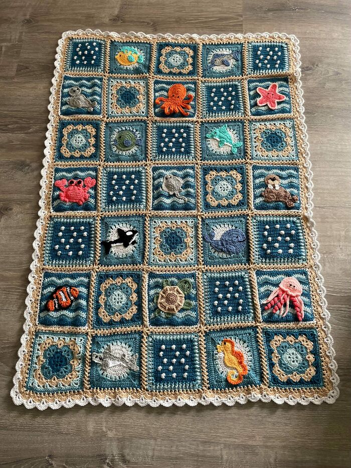 Crocheted ocean-themed blanket with animal and floral motifs on wooden floor