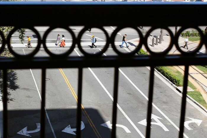Perfectly timed street photo by Jeremy Paige from above, showing pedestrians crossing a street through a fence.