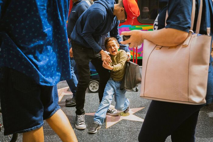 A perfectly timed street photo by Jeremy Paige, of a child crying while being held by an adult on a street.