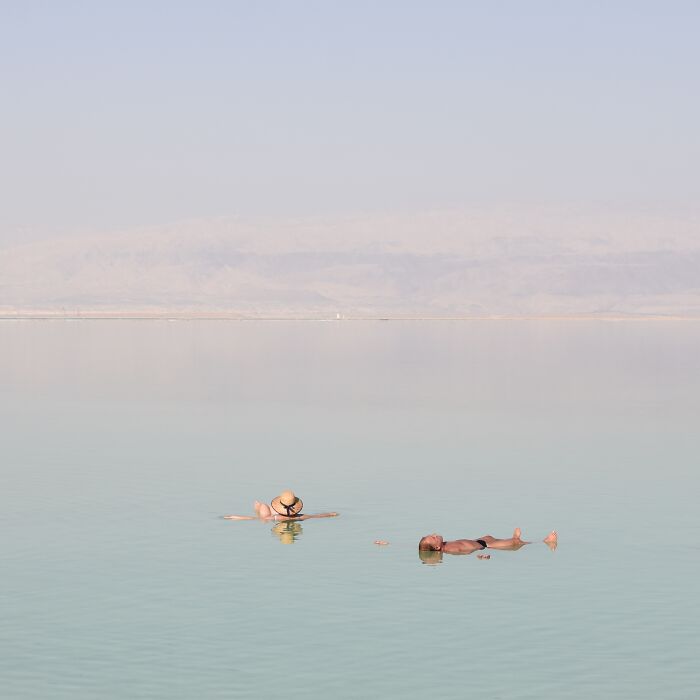 Two people float on their backs in still, vast water, showcasing minimalist art from a beach scene with negative space.