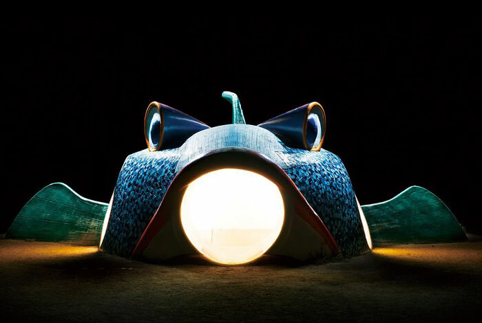 Surreal Japanese playground at night featuring a fish-shaped slide with glowing eyes and mouth, captured by Fujio Kito.