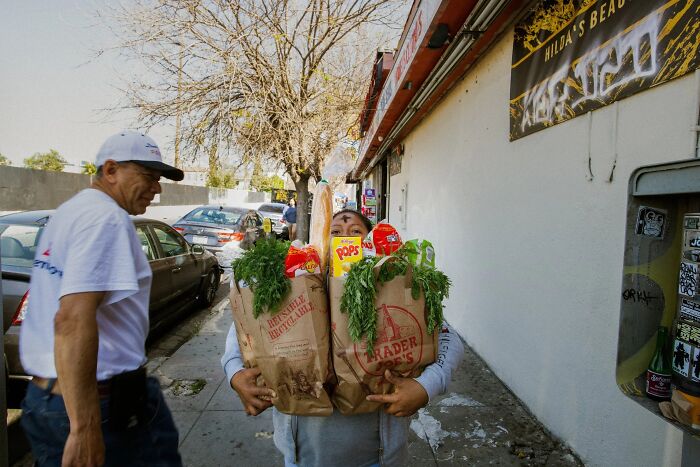 A perfectly timed street photo by Jeremy Paige of a person holding two full grocery bags in front of a store.