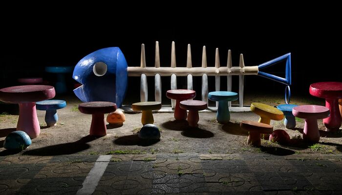 A surreal fish skeleton sculpture and colorful stools in a Japanese playground at night, by Fujio Kito, looking like another world scene.