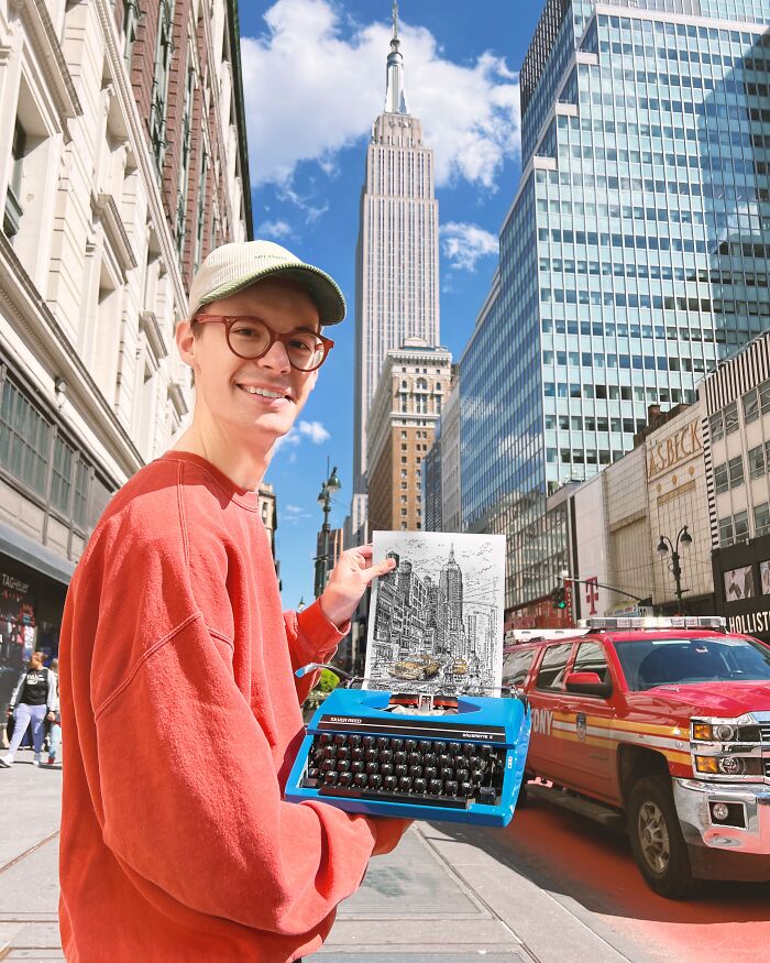 A man smiling and holding his typewriter art of the Empire State Building on a bustling city street.