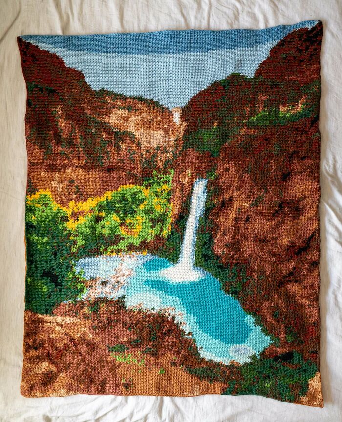 Crocheted blanket showing nature scene with waterfall and cliffs