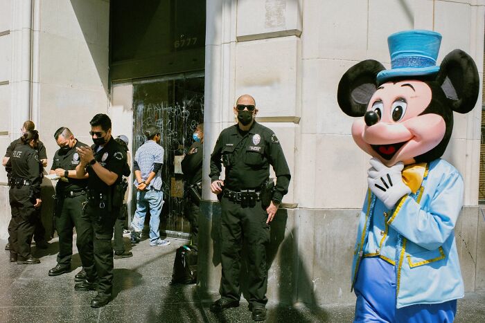 A perfectly timed street photo by Jeremy Paige, with a costumed character next to police officers.
