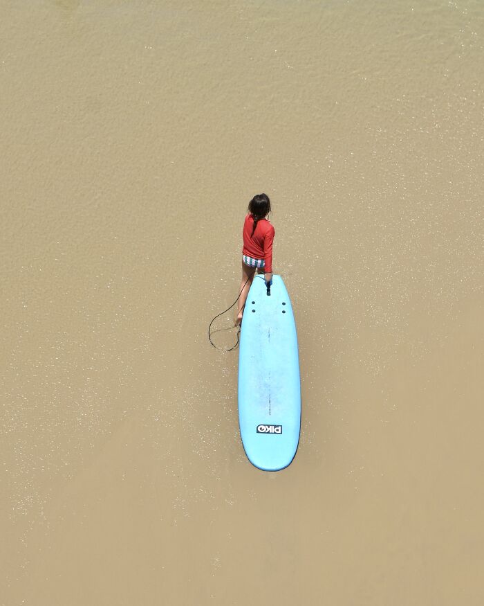 A photographer uses negative space to capture a child with a surfboard on a minimalist beach.