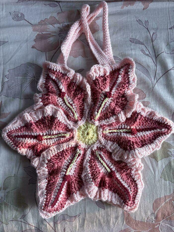 Pink and red crocheted flower-shaped bag with handles on bedspread