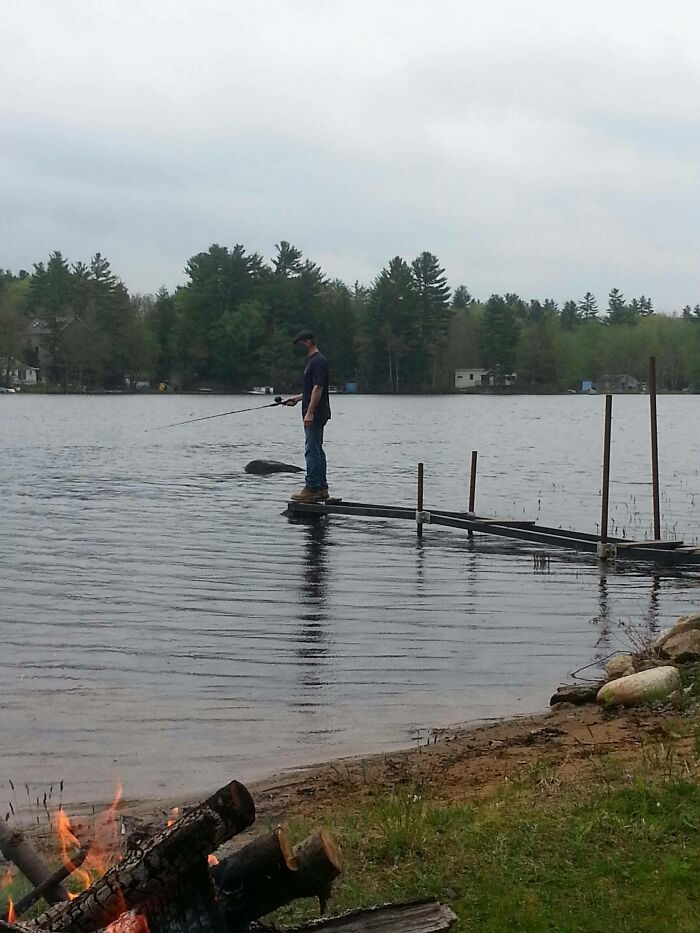 A man precariously standing on a partially submerged dock section, illustrating a DIY fail from someone whose confidence outpaced their skills.