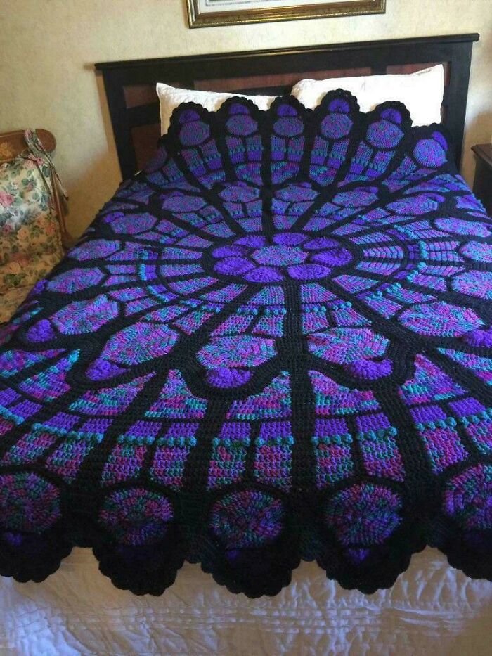 Purple and black crocheted blanket with stained glass window design on bed