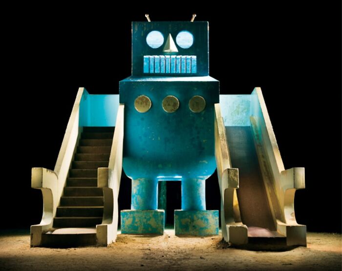Surreal Japanese playground at night featuring a blue robot slide structure by Fujio Kito.