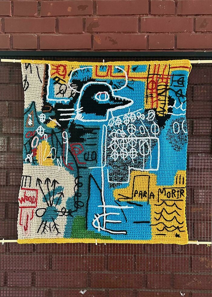 Crocheted art piece with abstract graffiti-style design on brick wall