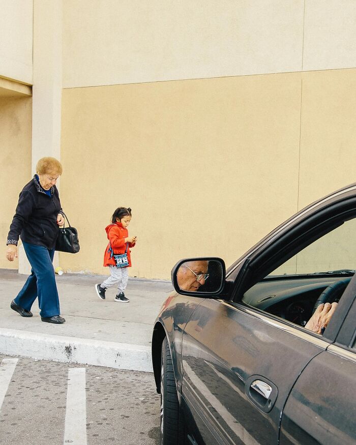 A woman and a child walking on a sidewalk, reflected in a car mirror, a perfectly timed street photo by Jeremy Paige.