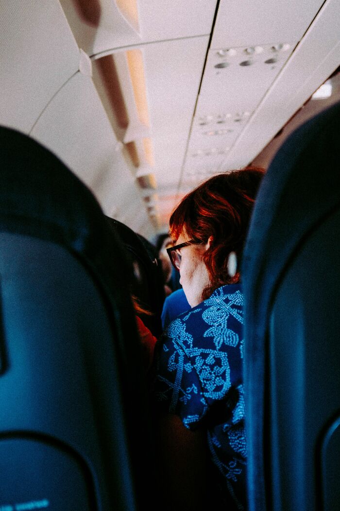 Entitled people on a plane. A woman with red hair wearing glasses, looking forward, needs a reality check.