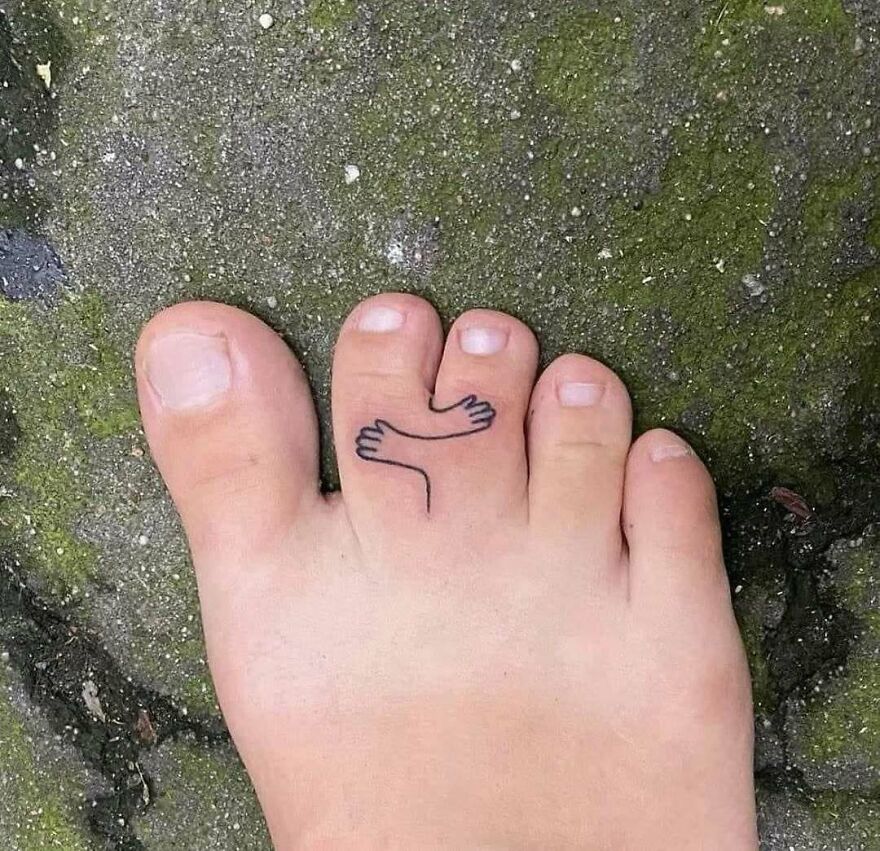 A close-up of a foot with a small tattoo of two hands hugging on one toe, an uncomfortable and disturbing pic.