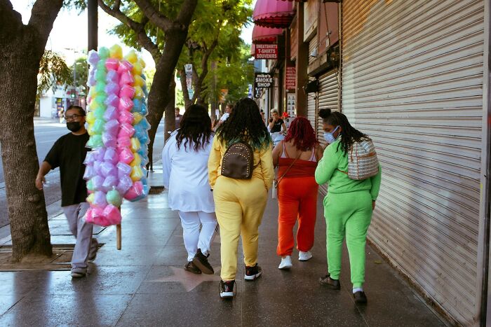 A vendor with colorful cotton candy walks past women on a Hollywood street, a perfectly timed street photo by Jeremy Paige.