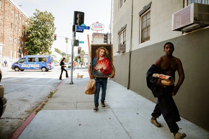 A man carries a large painting on a busy street, one of the perfectly timed street photos by Jeremy Paige.