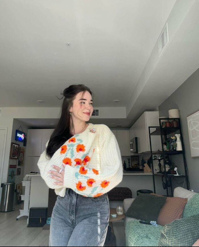 Woman wearing cream crochet sweater with orange and blue flower patterns