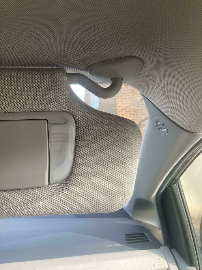 A car interior with a bent sun visor hook, a hilariously unhinged design fail.