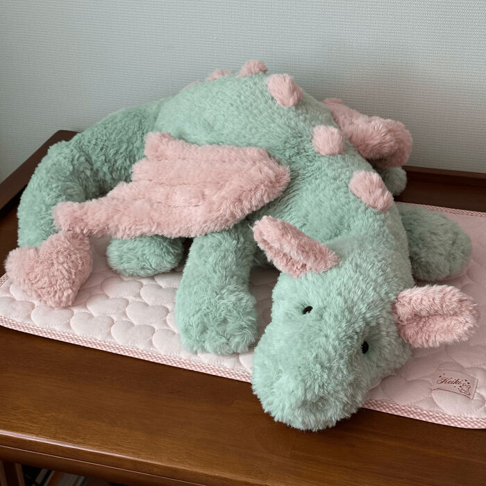 Soft crocheted dragon plush in pastel green and pink resting on a quilted mat