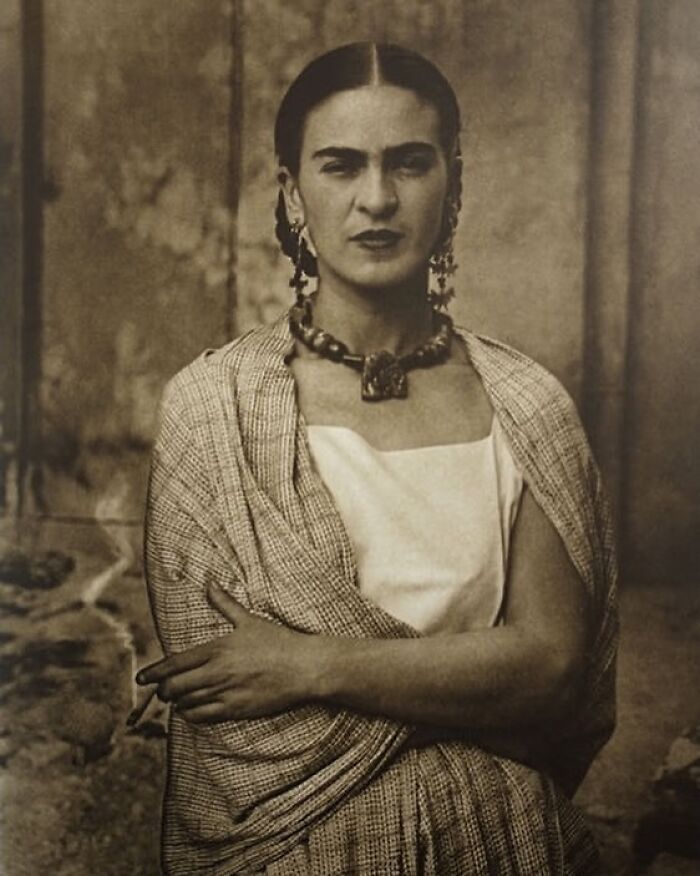A prominent woman in history, Frida Kahlo, gazes directly with a serious expression.