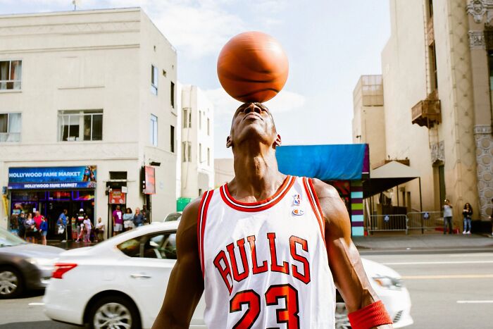 A perfectly timed street photo by Jeremy Paige of a man in a Bulls jersey balancing a basketball on his head.