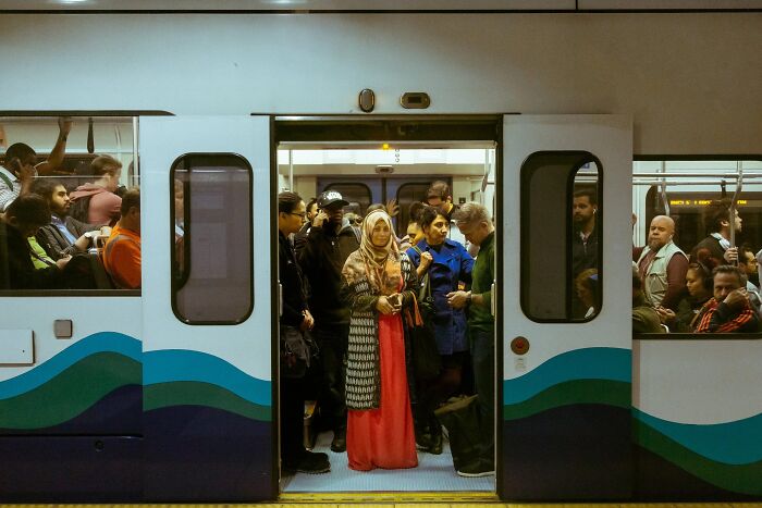 A perfectly timed street photo by Jeremy Paige captures people waiting to board a busy train, with one woman in a red dress.