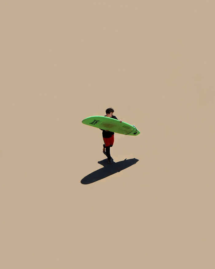 Surfer walking on expansive sand with a green surfboard, minimalist art beach scene with negative space.