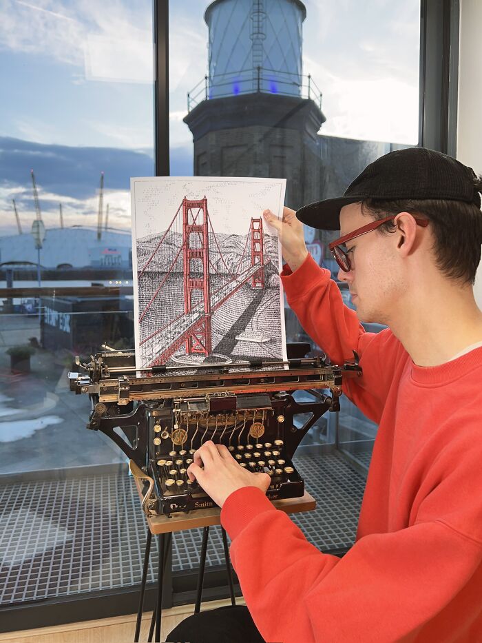 A man creates typewriter art of the Golden Gate Bridge, with a lighthouse and cityscape in the background.