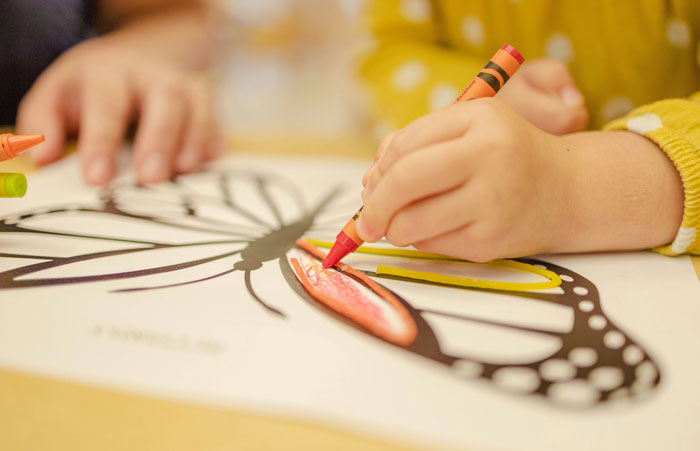 Child coloring a butterfly drawing with crayons