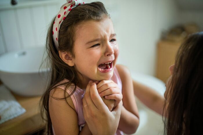 A young child crying intensely while an adult's hands comfort them.