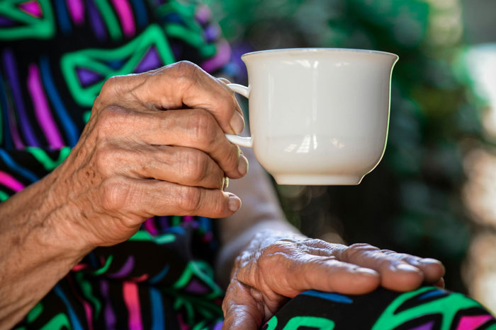 Elderly hand holding a cup with vivid colorful clothing background