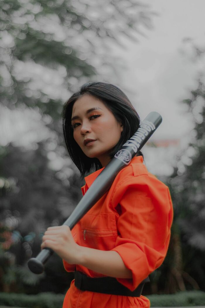 Young woman in an orange jumpsuit holding a baseball bat, embodying self-protection for women living alone.