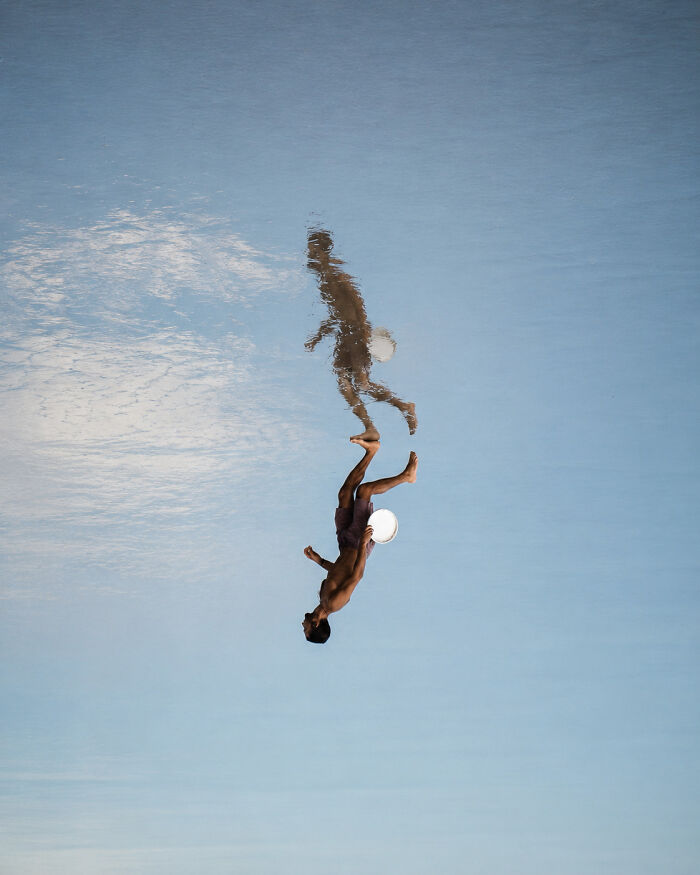 Man diving reflected in calm water, a minimalist art beach scene using negative space by a photographer.