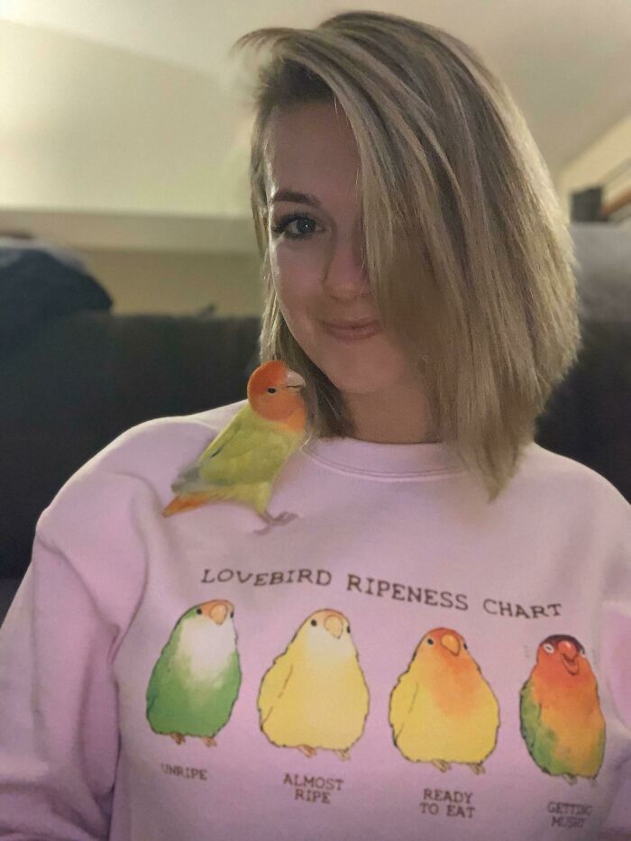 A woman with a lovebird on her shoulder, wearing a shirt showing lovebird ripeness, humorously related to forbidden foods.