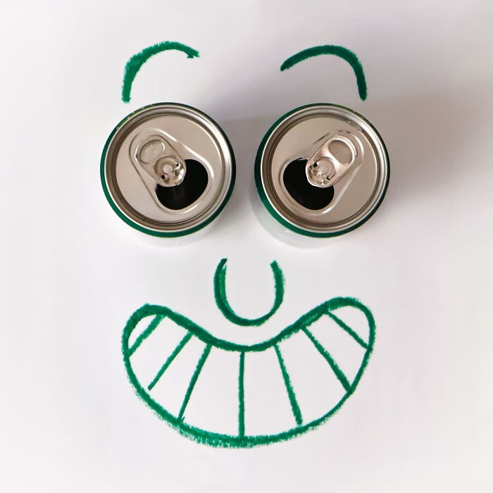 Two aluminum cans used as eyes for a drawn smiling face in a playful illustration of everyday objects.