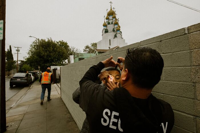 Jeremy Paige captures a perfectly timed street photo of a security guard checking a man's eyes near a church.