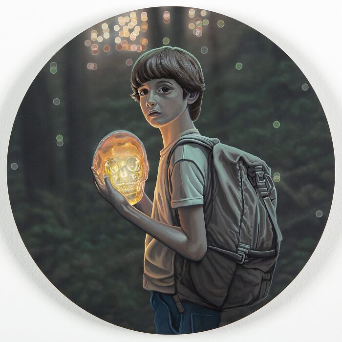 Surreal paintings by Wiley Wallace: A young boy holds a glowing skull in a dark forest, with bokeh lights in the background.