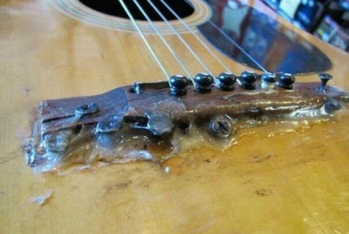 A DIY fail: a close-up of a guitar's bridge with excessive, melted glue showing a poor repair.