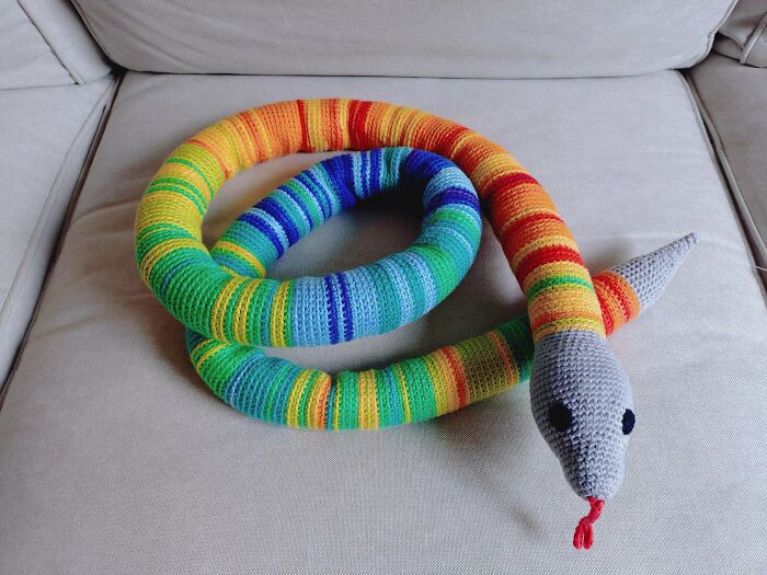 Colorful crocheted snake toy with vibrant stripes on sofa