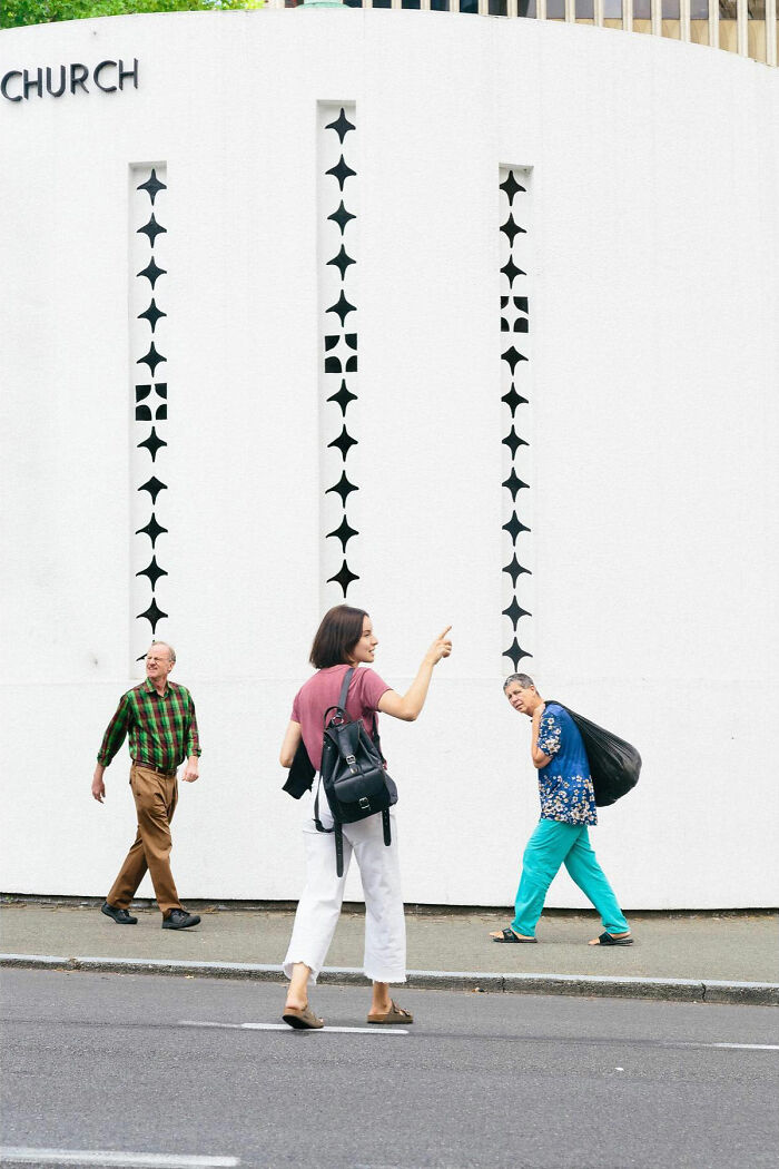 A perfectly timed street photo by Jeremy Paige of people walking past a white building with decorative windows.