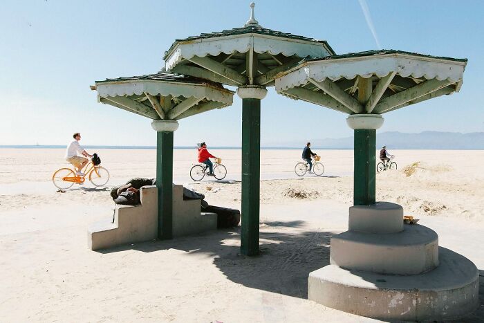 Perfectly timed street photo by Jeremy Paige of several people riding bicycles on a sunny beach path.