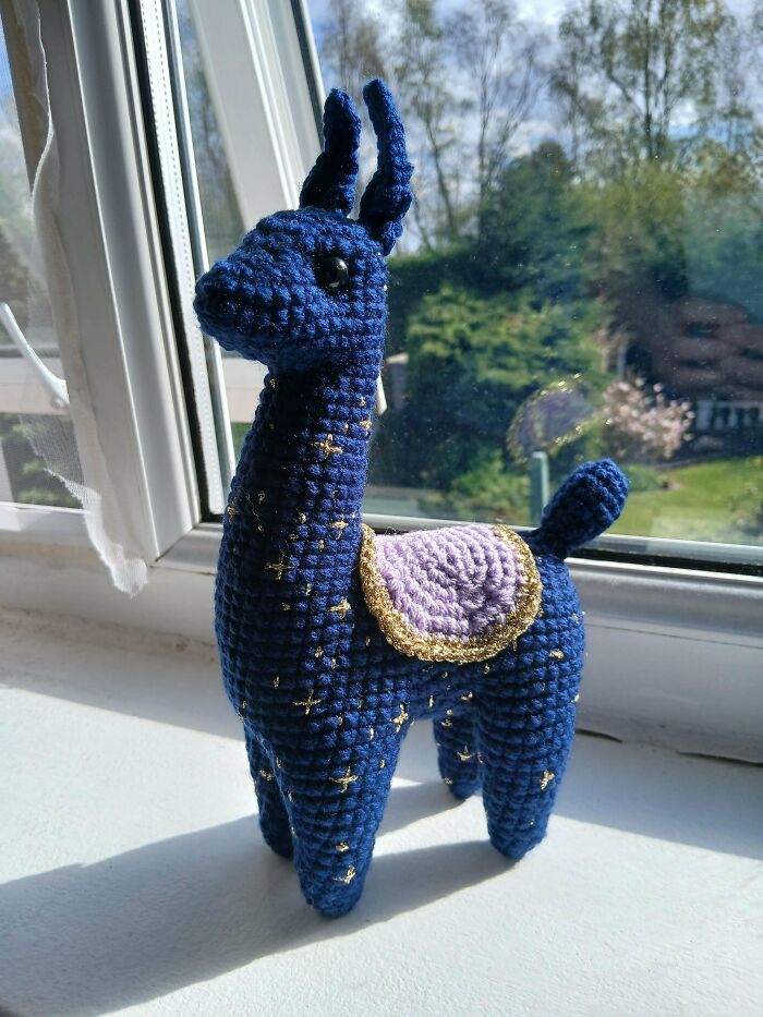 Blue crocheted llama amigurumi with gold accents and purple saddle