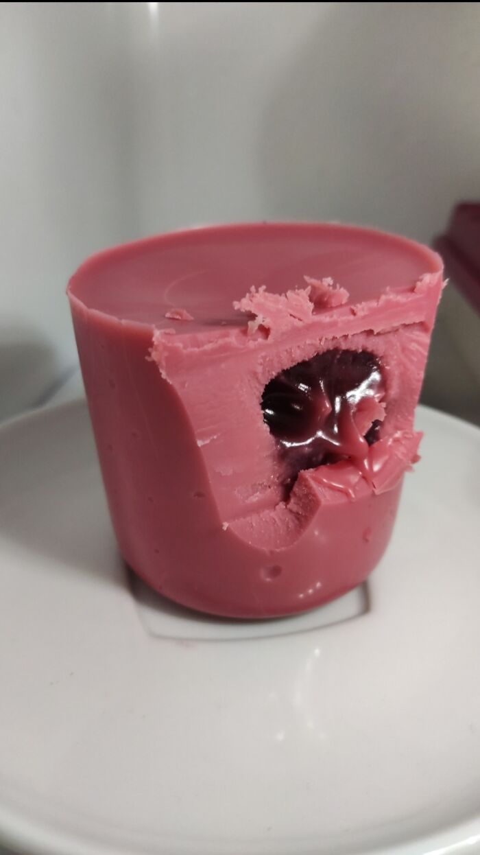 A partially eaten forbidden food, a pink cup-shaped treat with a gooey purple center, on a white plate.