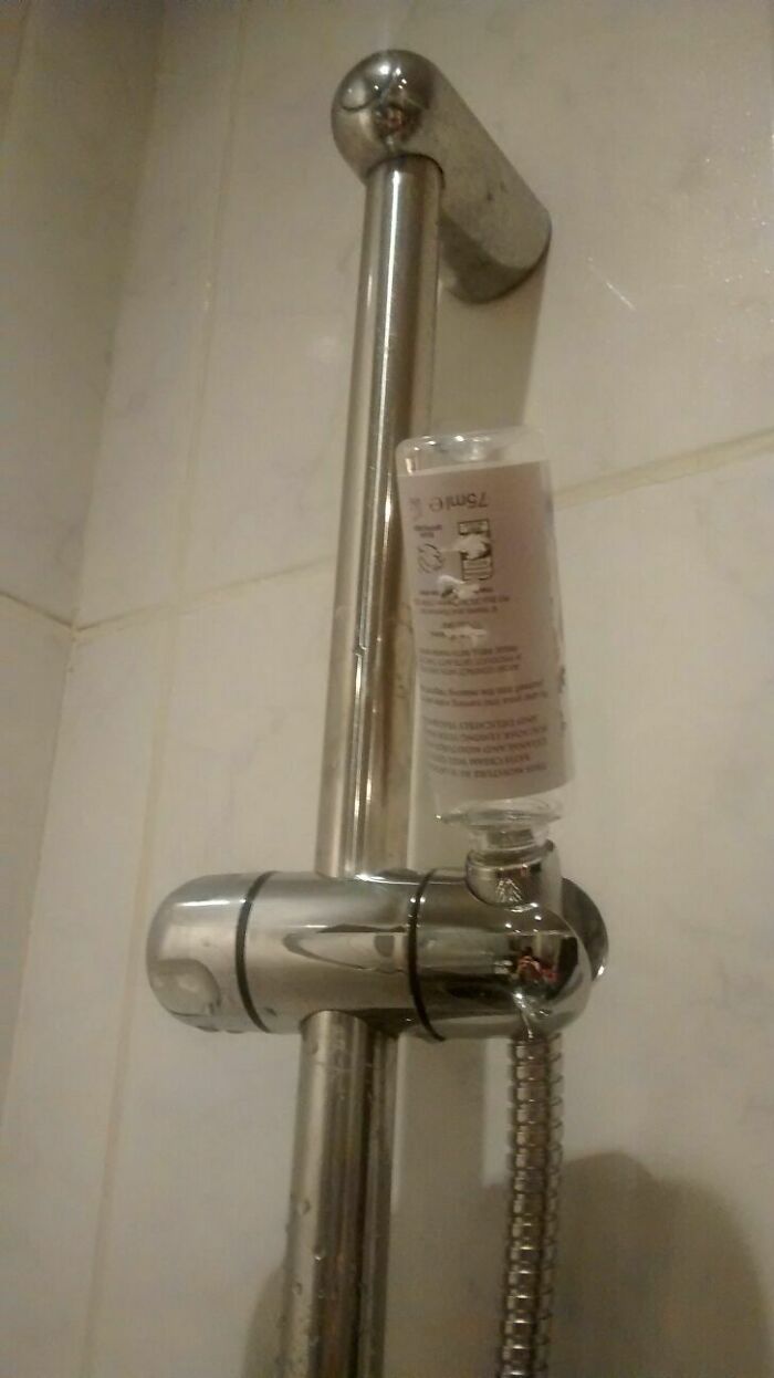 A DIY fail with a shampoo bottle precariously balanced on a shower rail, demonstrating a lack of proper storage.