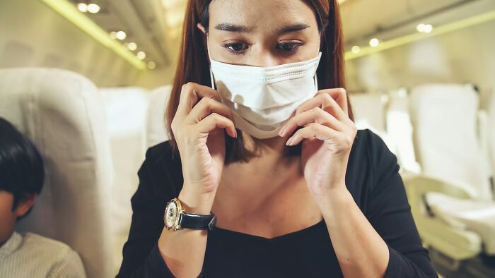 A passenger adjusts her mask on an airplane, highlighting things cabin crew deal with.